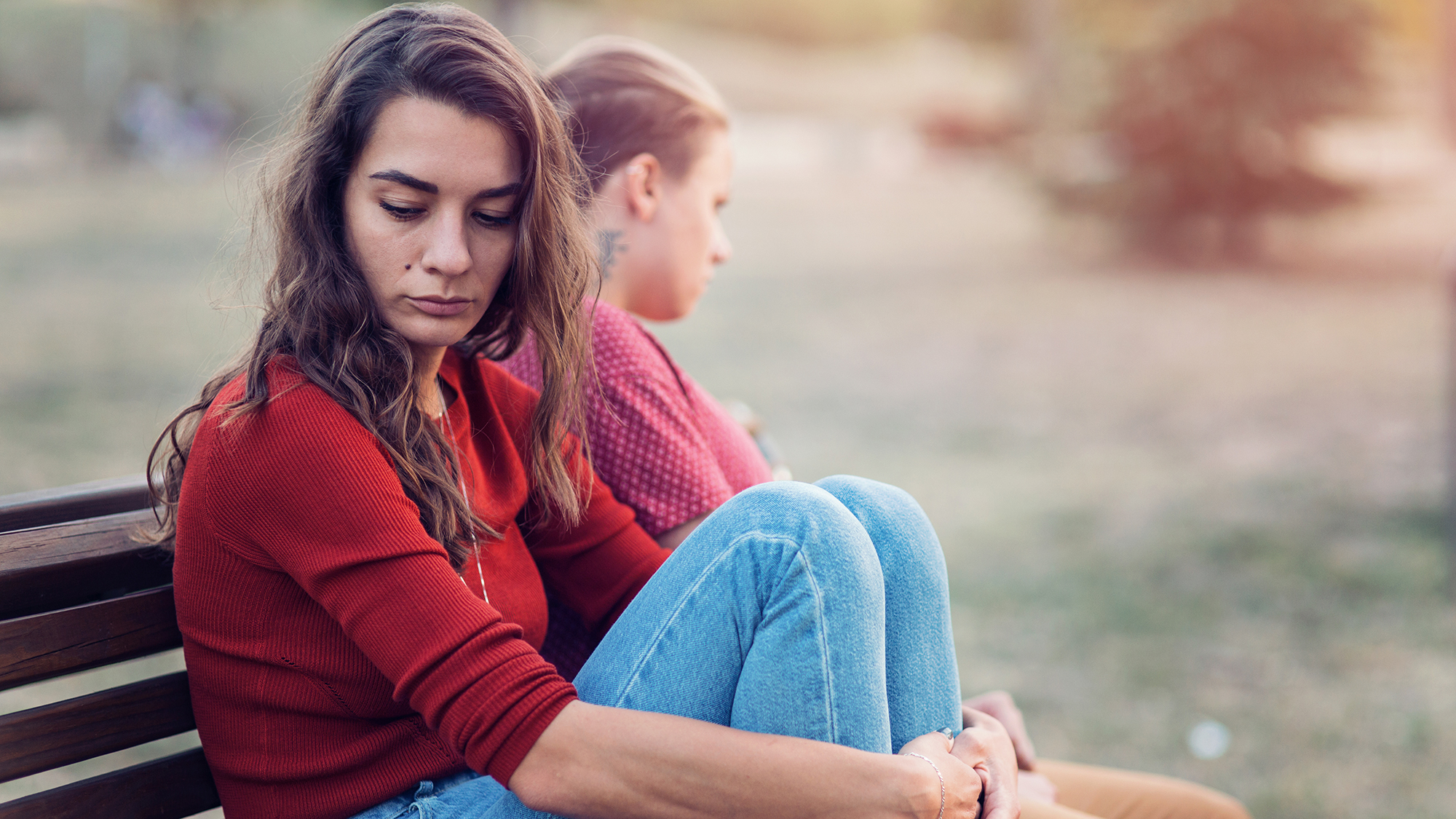 Mädchen und Bursch sitzen traurig auf einer Parkbank