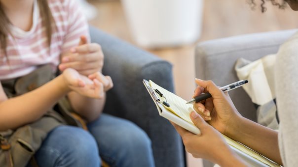 Mädchen sitzt Frau gegenüber welche sich Notizen macht