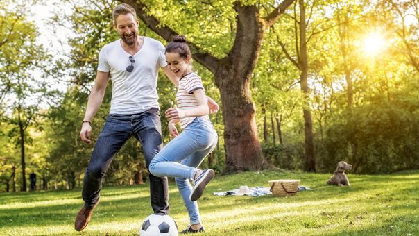 Vater spielt mit Tochter Fußball im Park
