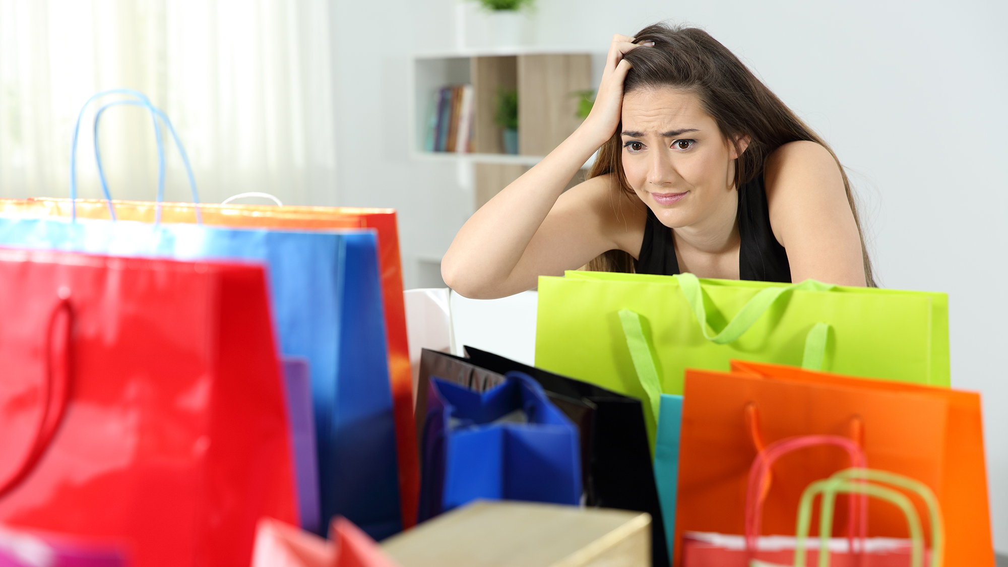 Frau sitzt verzweifelt vor vielen Einkaufstaschen