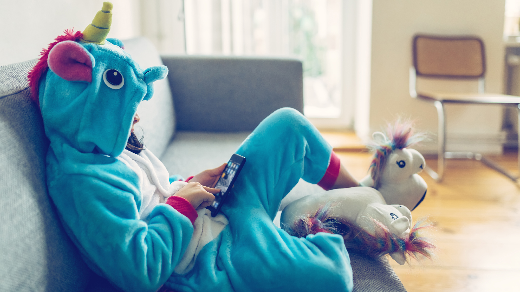 Mädchen sitzt alleine in Einhornkostüm mit Handy auf dem Sofa