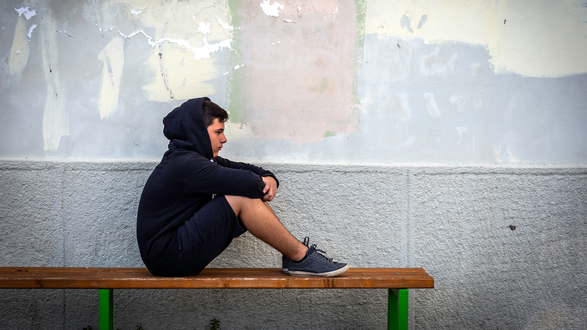Junge sitzt traurig und alleine auf einer Bank