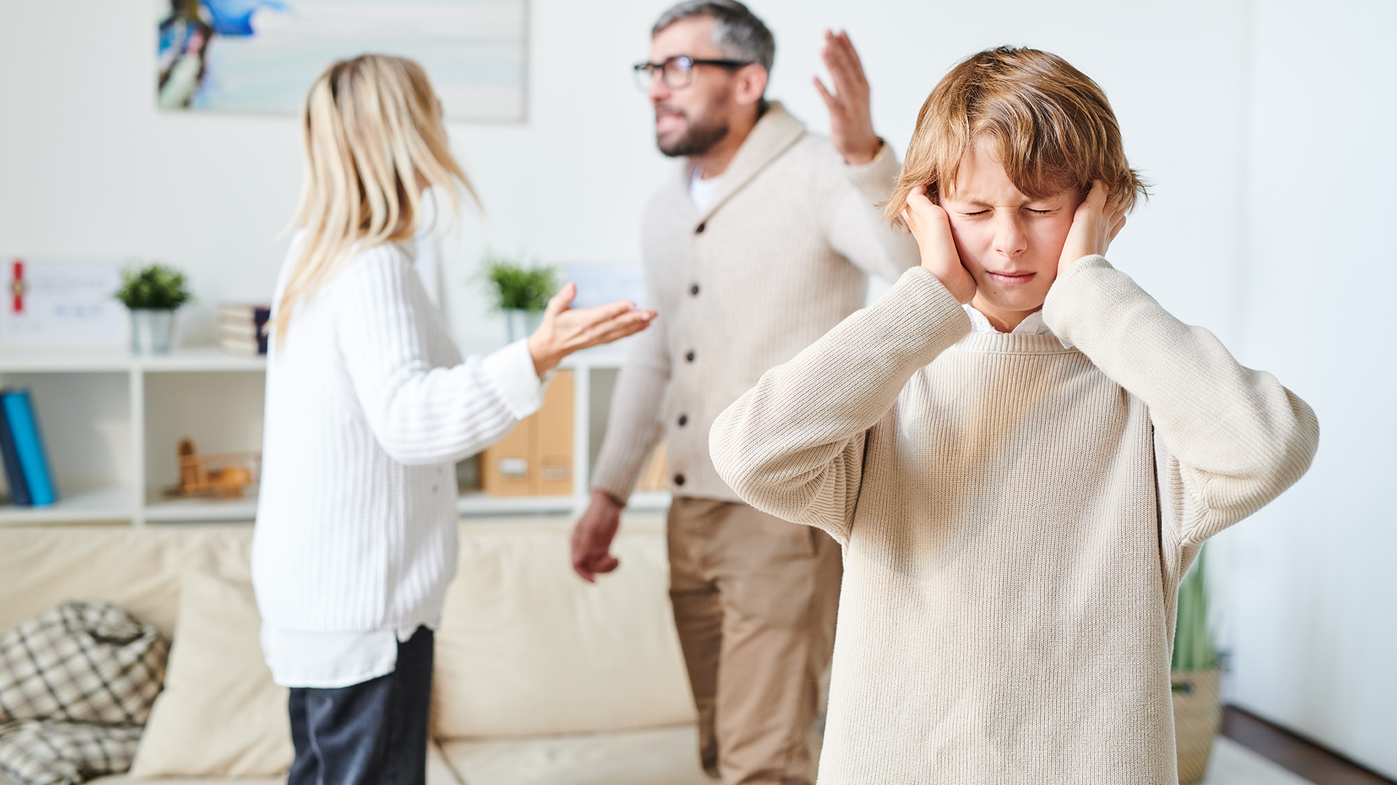 Junge hält sich Ohren zu, im Hintergrund streiten Eltern