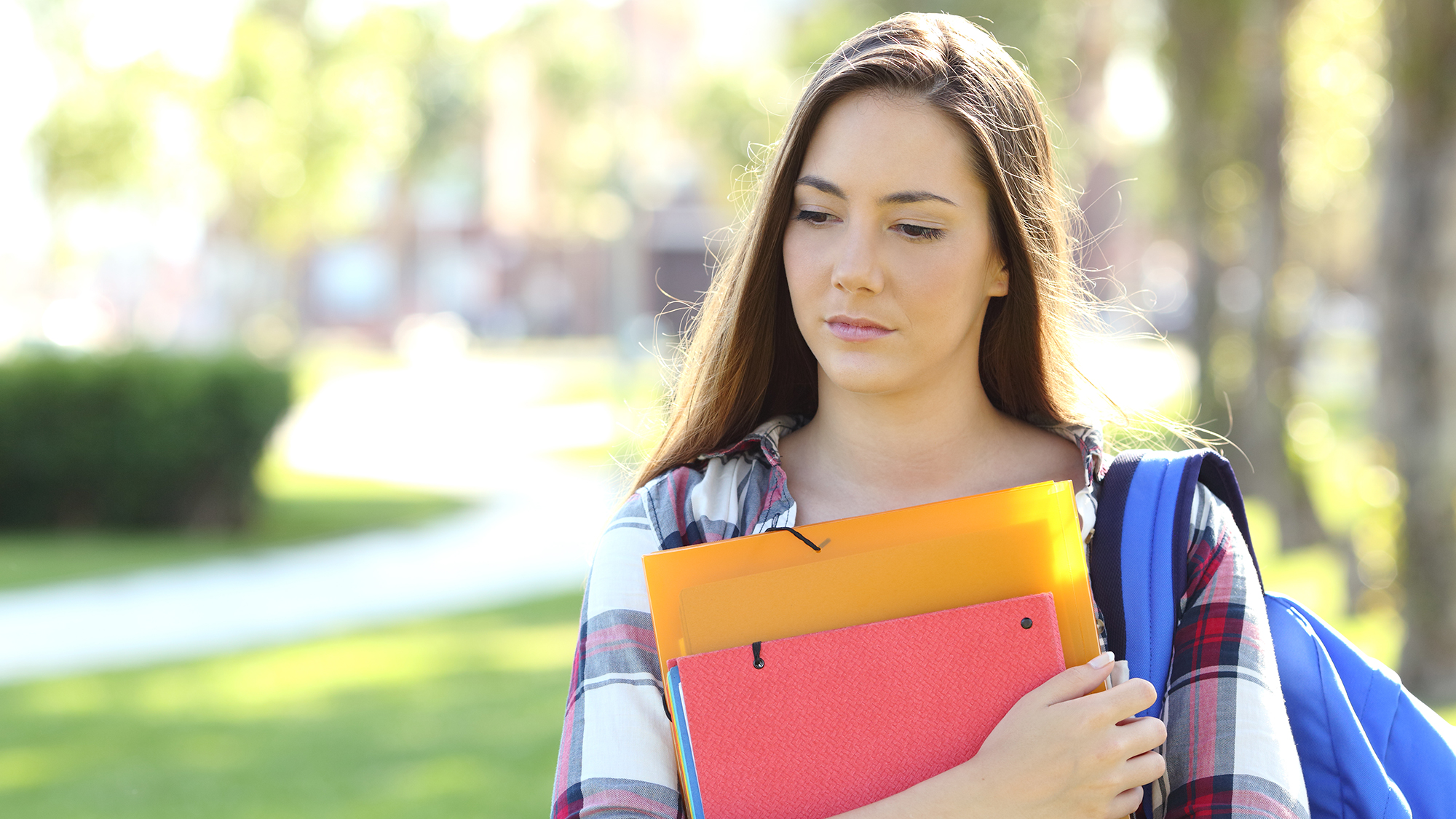 Ein Mädchen hält seine Schulsachen und geht traurig über das Schulgelände