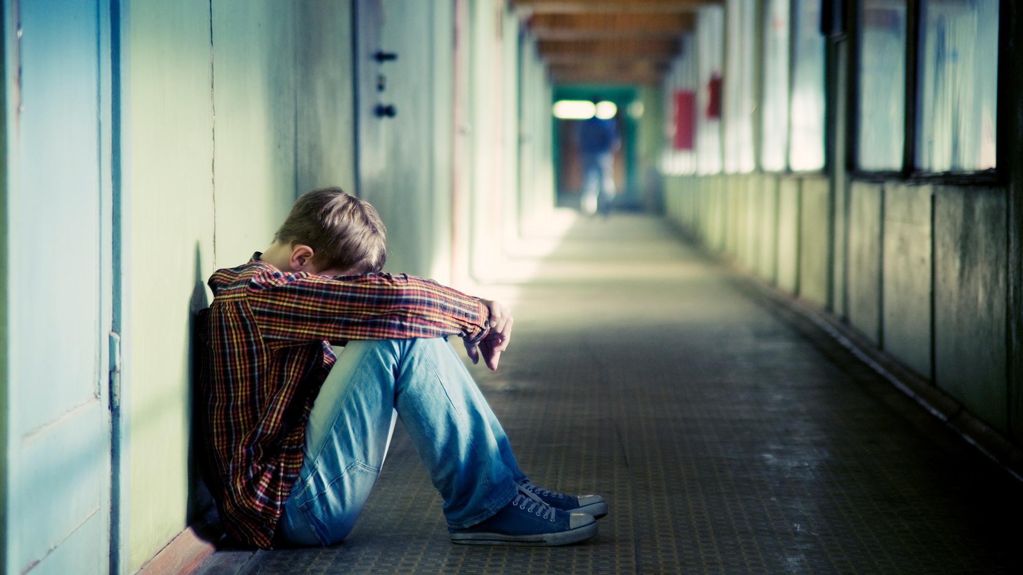 Junge sitzt am Boden im Schulgang