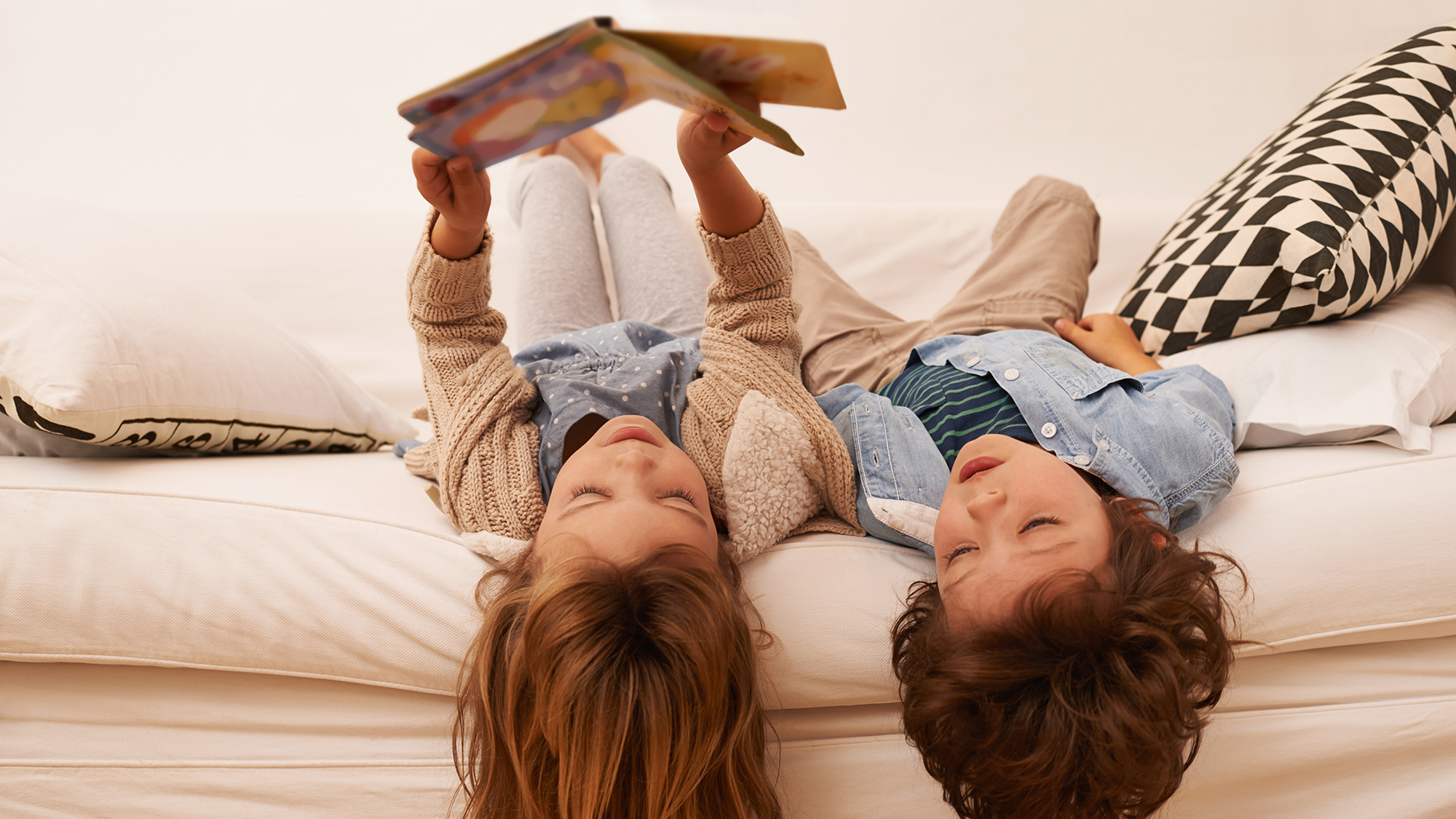 Geschwister liegen auf dem Bett und lesen gemeinsam