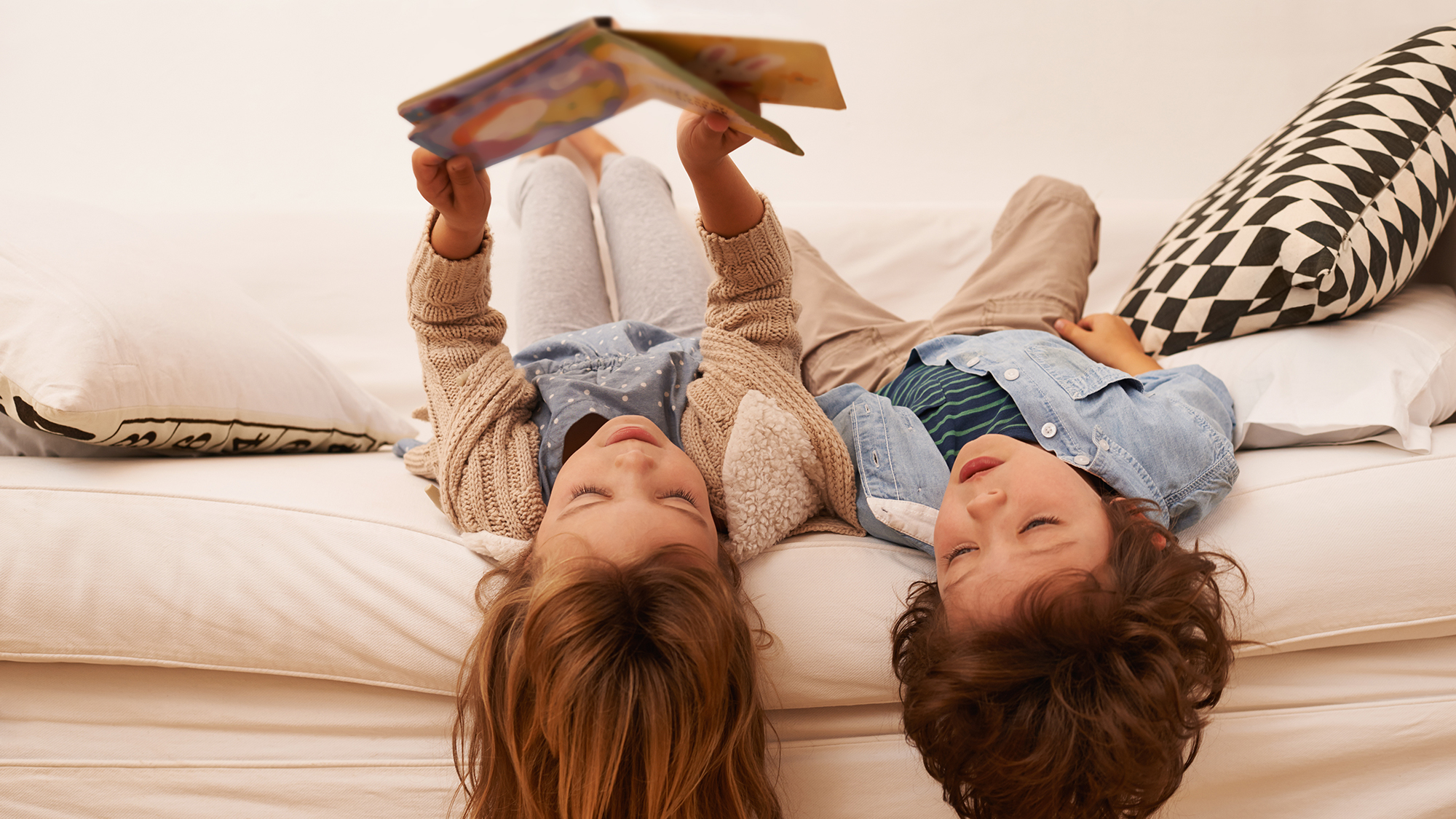 (c) iStockphoto.com/PeopleImages Geschwister liegen auf dem Bett und lesen gemeinsam