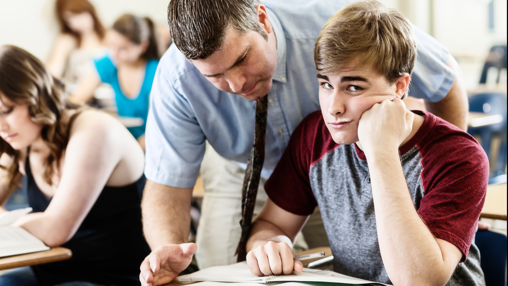 Junge schaut genervt während Lehrer über Tisch lehnt