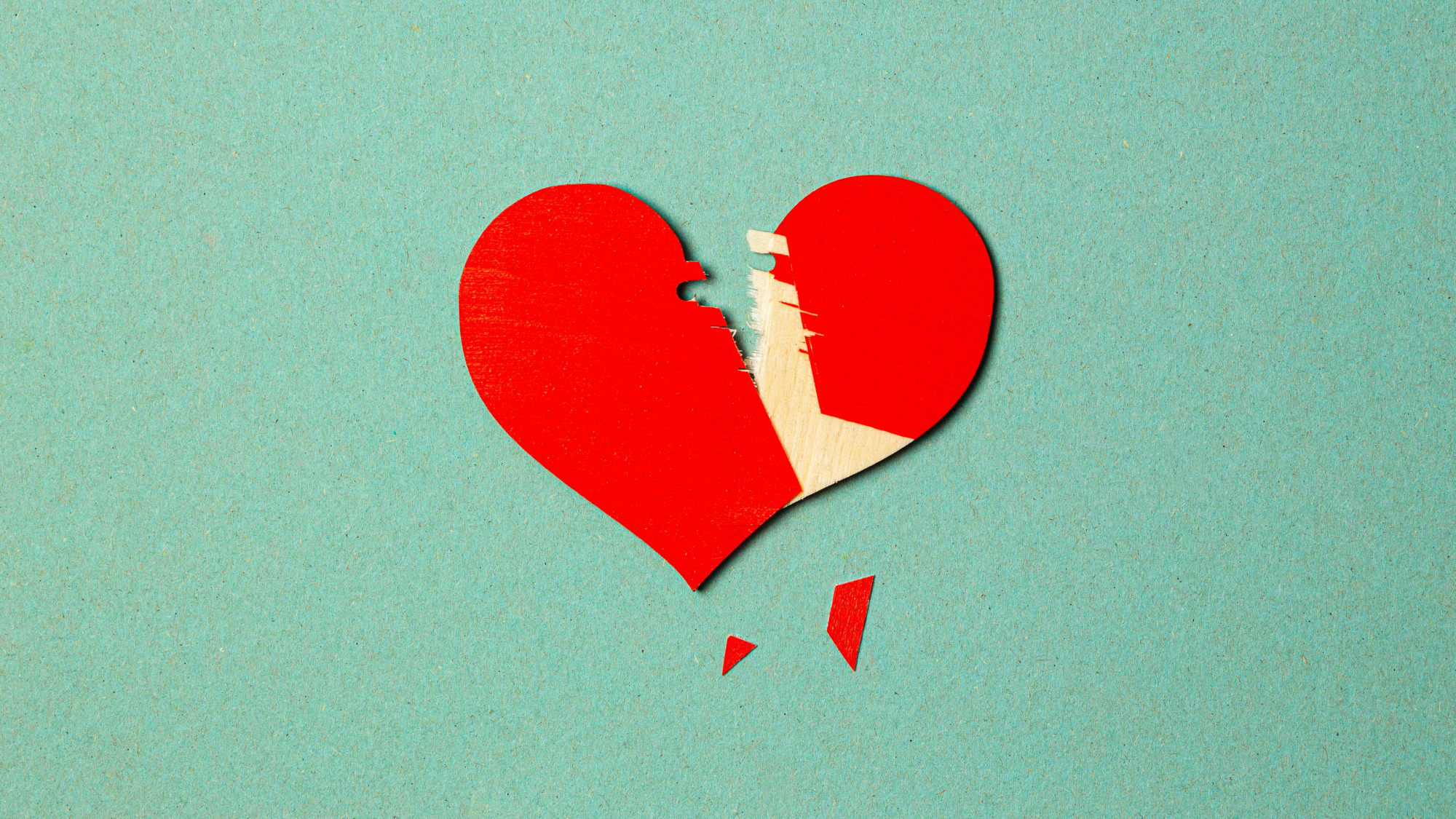 Zerbrochenes rotes Herz auf türkisem Hintergrund.