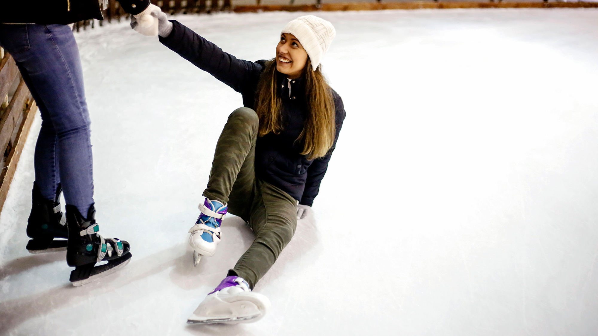 Ein Mädchen liegt auf der Eisfläche, ein anderes Mädchen hilft ihr auf