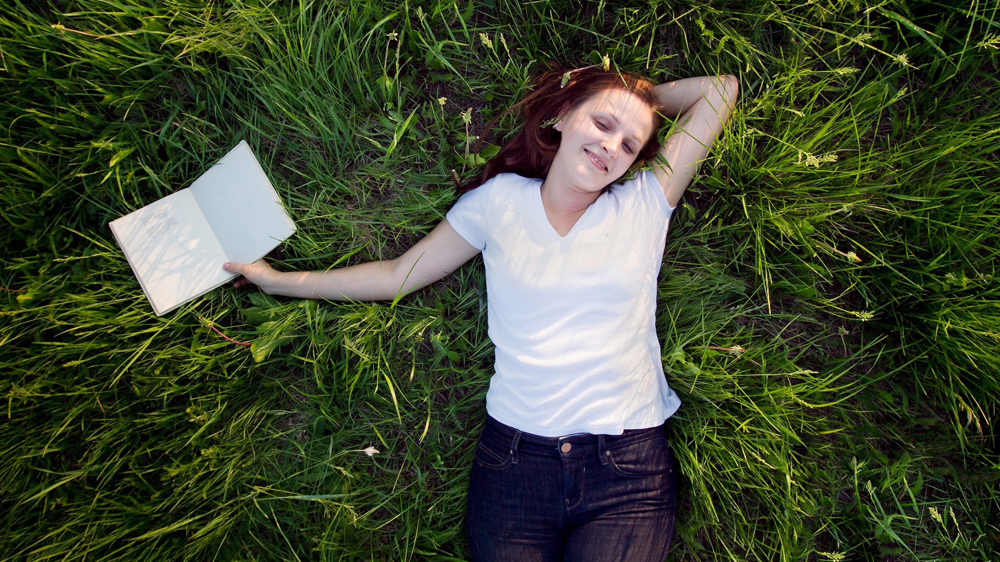 Mädchen liegt mit Buch auf der Wiese