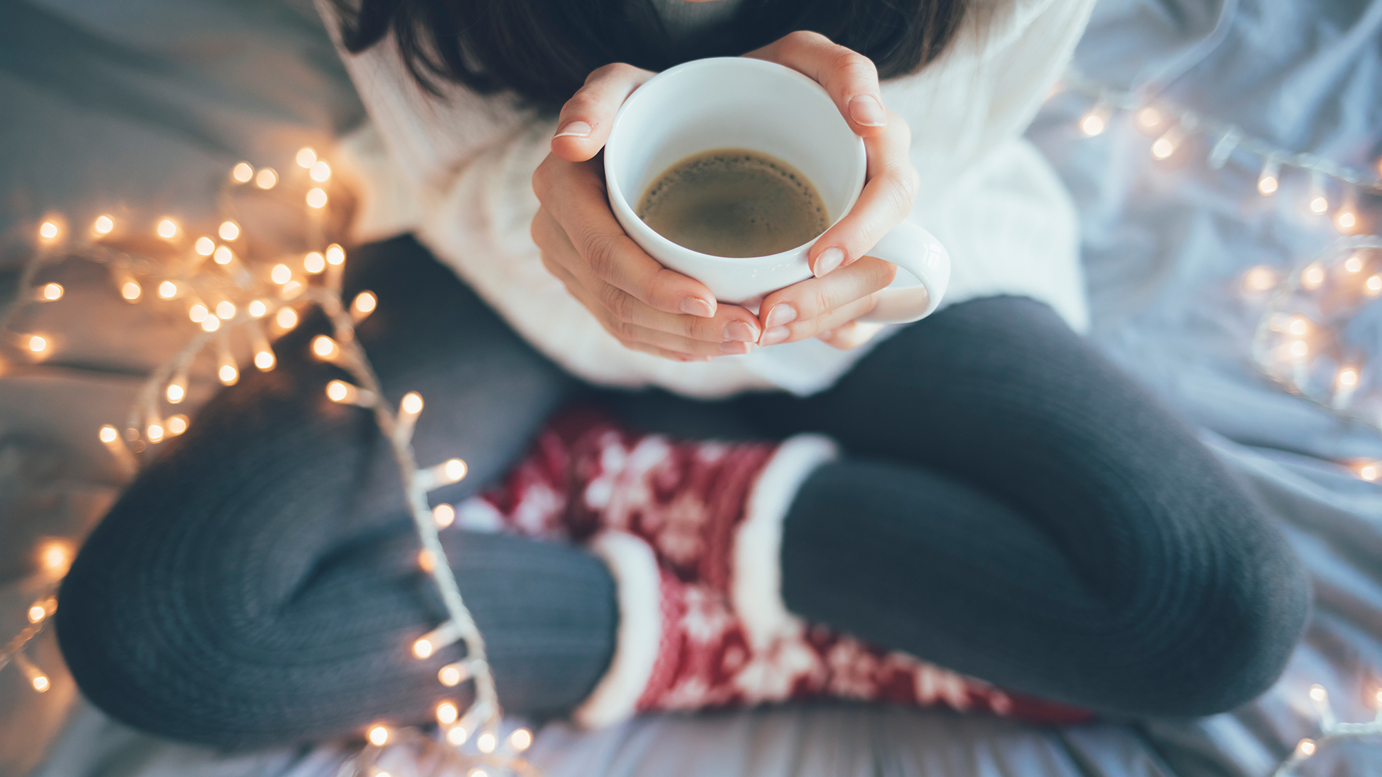Mädchen sitzt auf Couch mit Lichterkette und einer Tasse Tee
