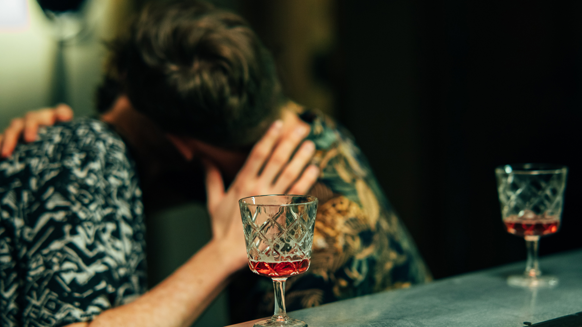 Burschen küssen sich in einer Bar. Auf der Bar stehen 2 Gläser Rotwein.