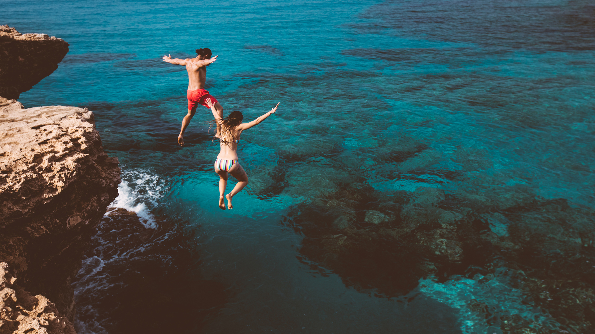 Bursch und Mädchen springen von einem Felsen ins Wasser