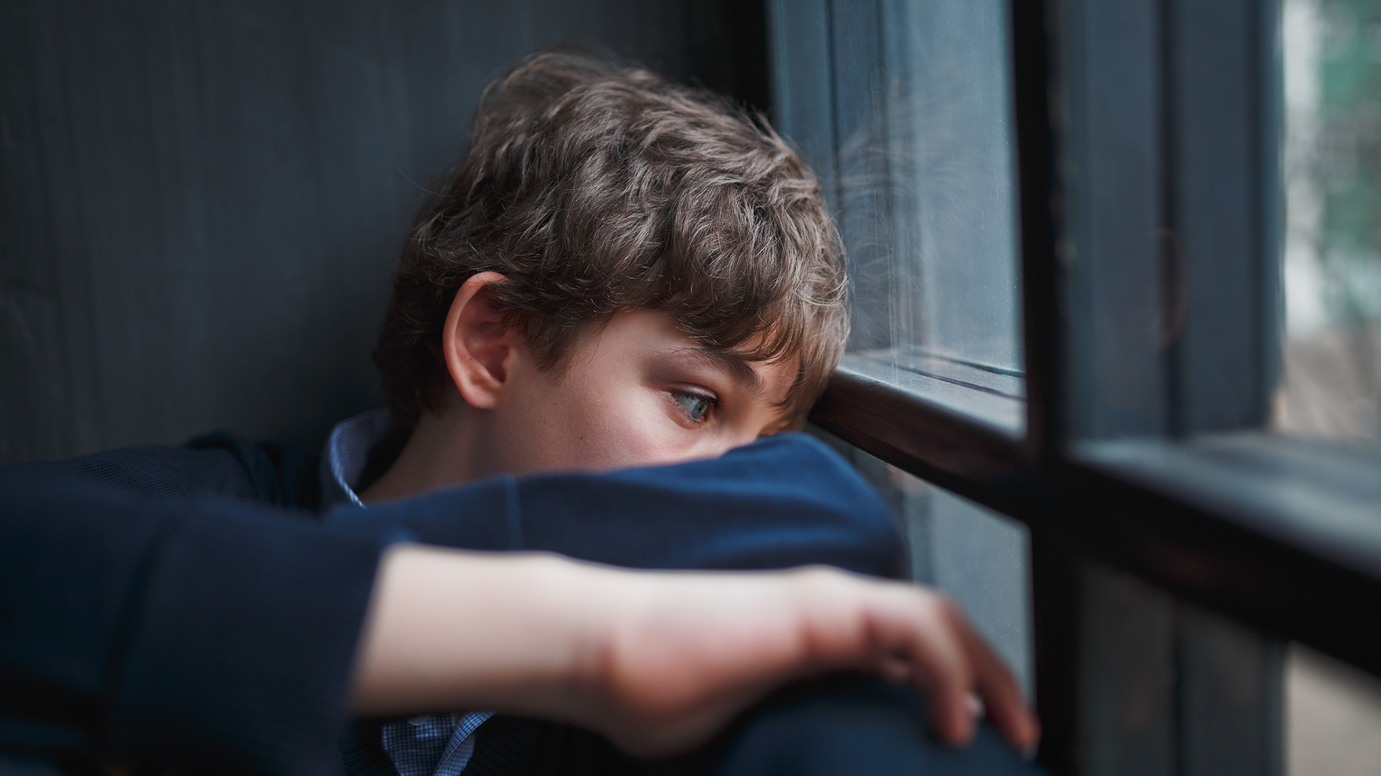 Junge sitzt traurig am Fenster